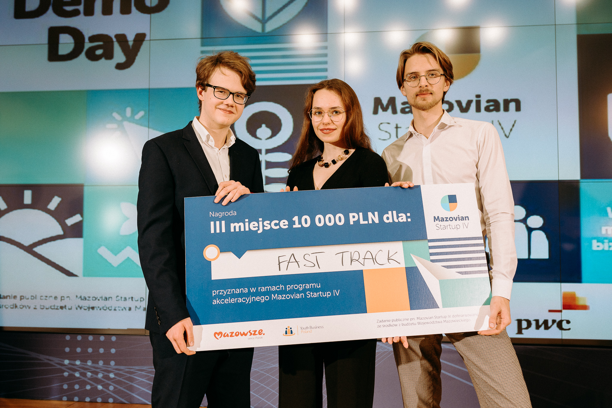 Troje młodych ludzi (dwóch mężczyzn i jedna kobieta), trzymający przed sobą symboliczny czek na 10 000 zł. W tle prezentacja.